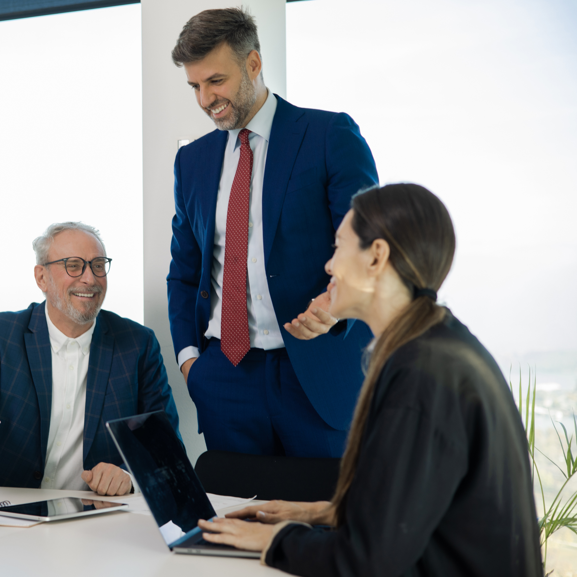 Three colleagues discussing their work around a laptop in a bright office.