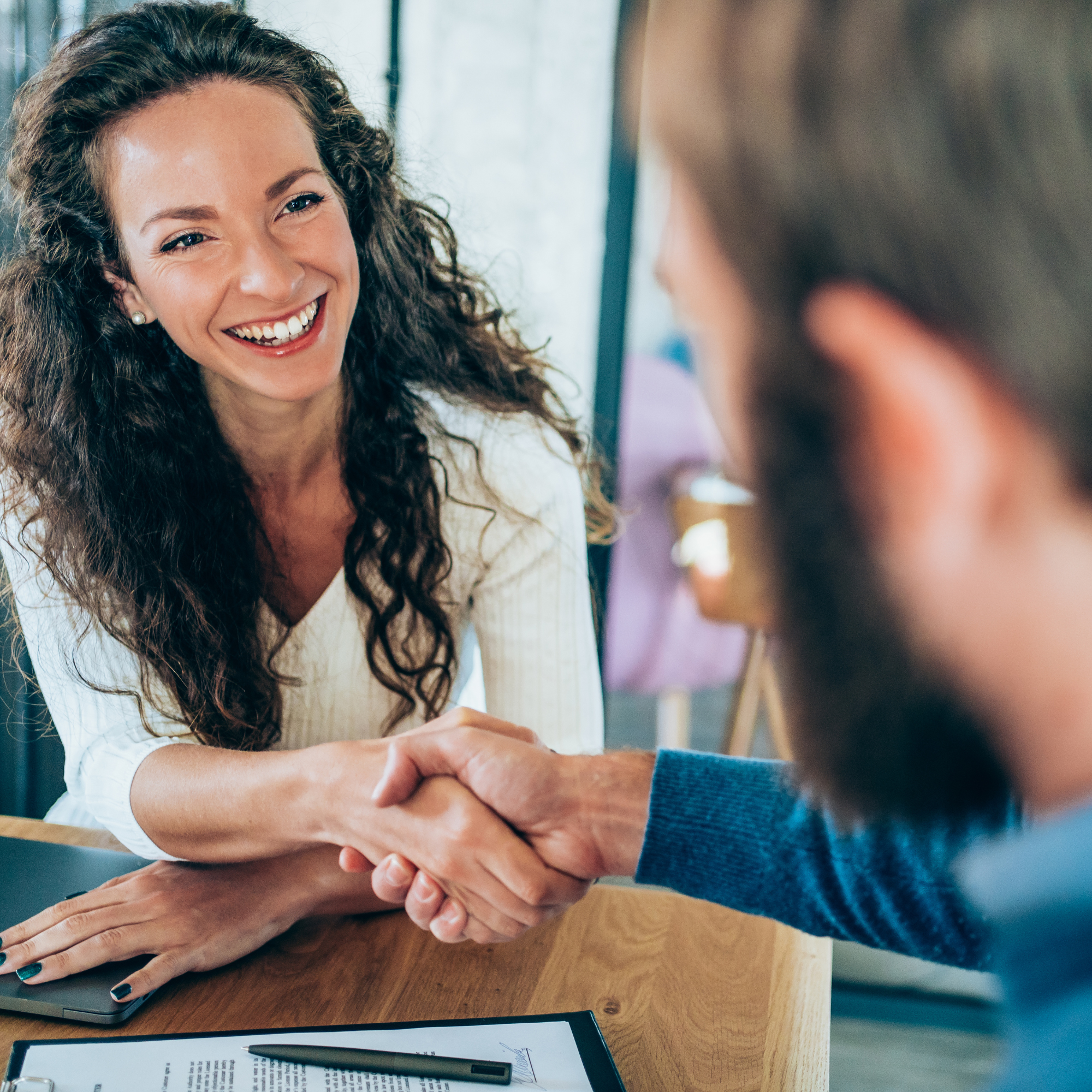 A professional greeting a colleague with a handshake across a table.