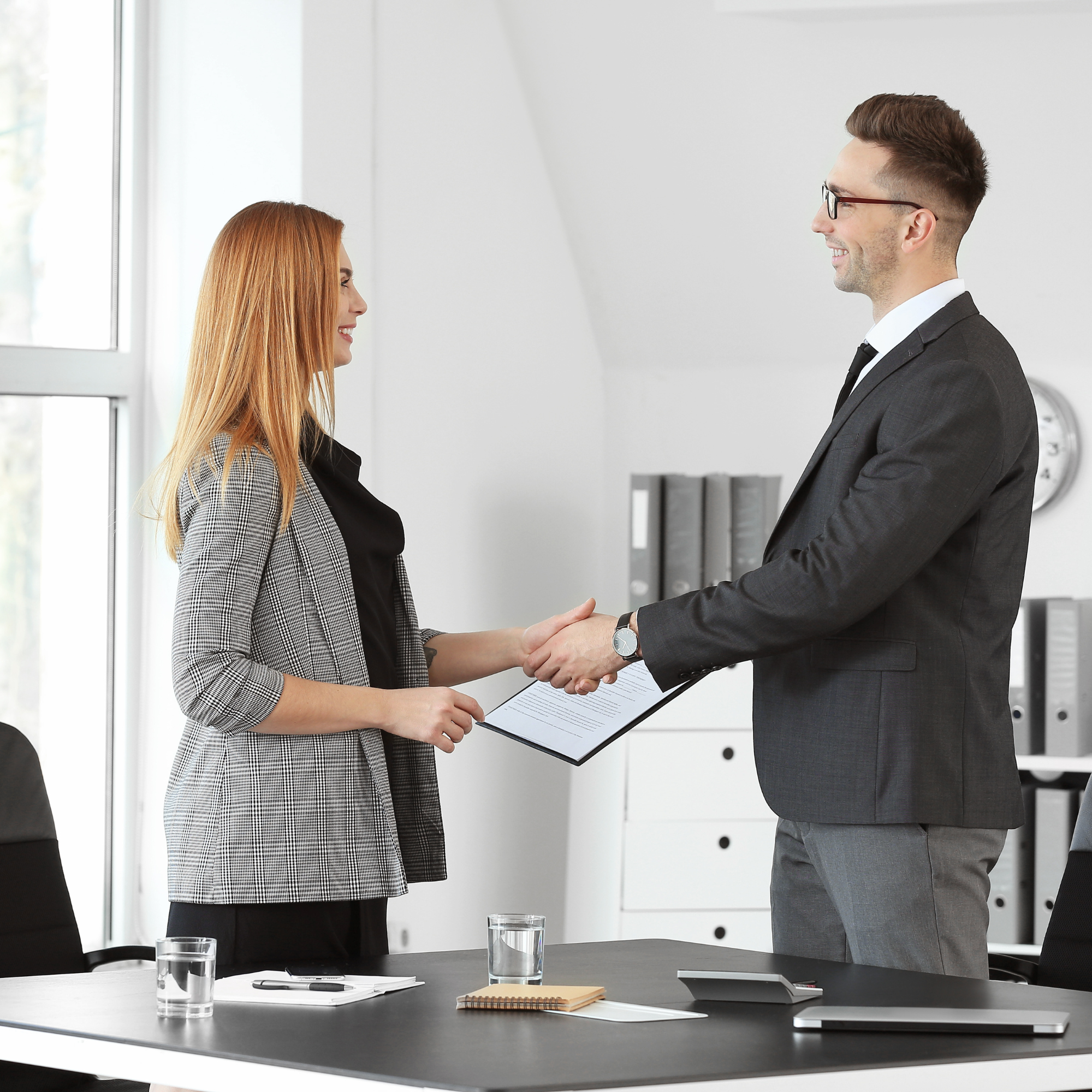 Two professionals shaking hands while holding a document.