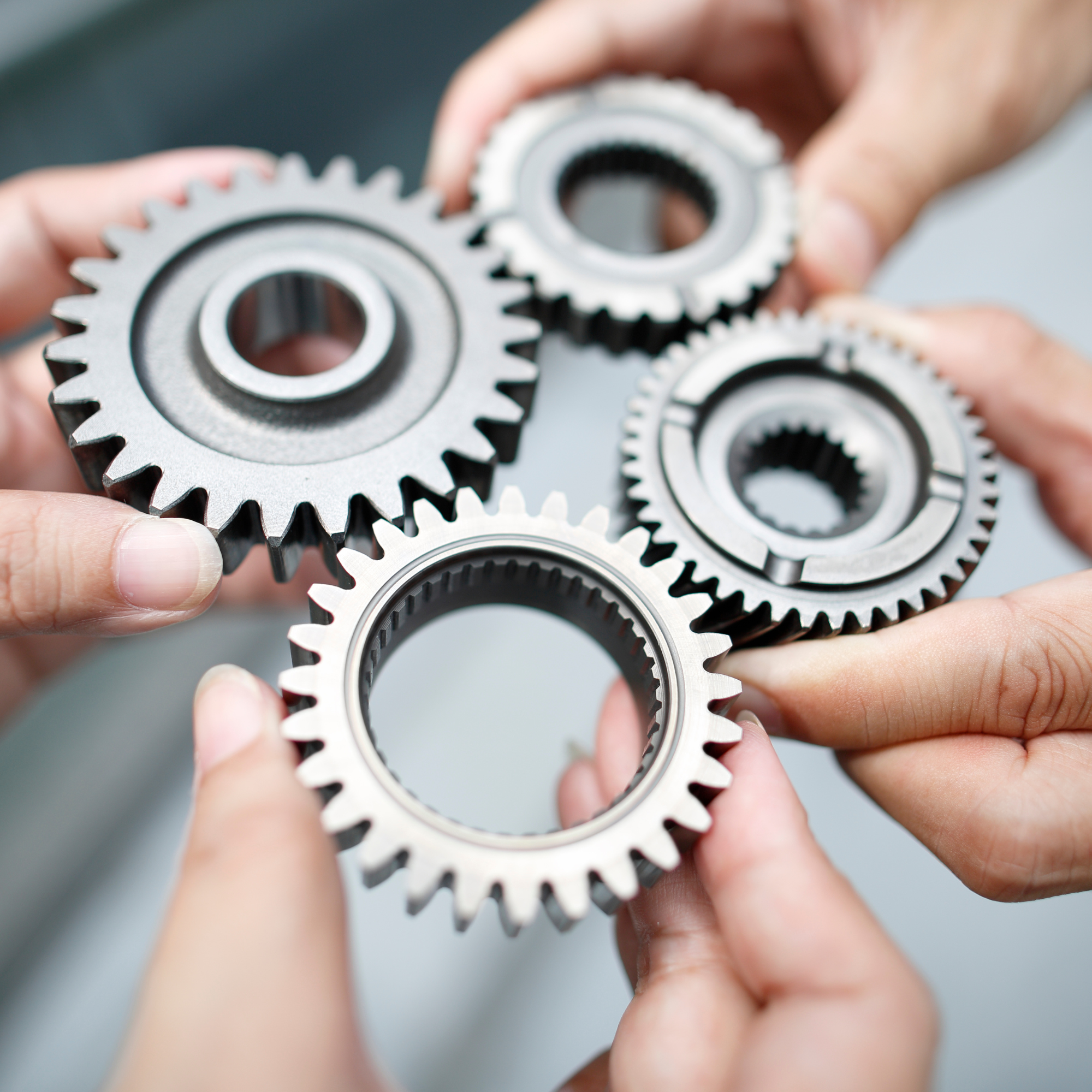 Hands bringing four interlocking metal gears together.